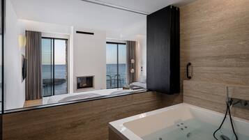 Une salle de bain moderne avec une baignoire, une douche en verre et une vue sur la mer grâce à de grandes fenêtres.