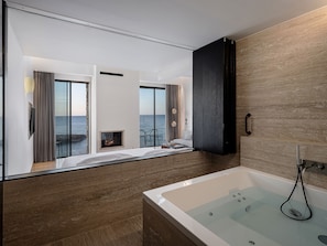 Un baño moderno con bañera, cabina de ducha de vidrio y vistas al mar a través de amplios ventanales.