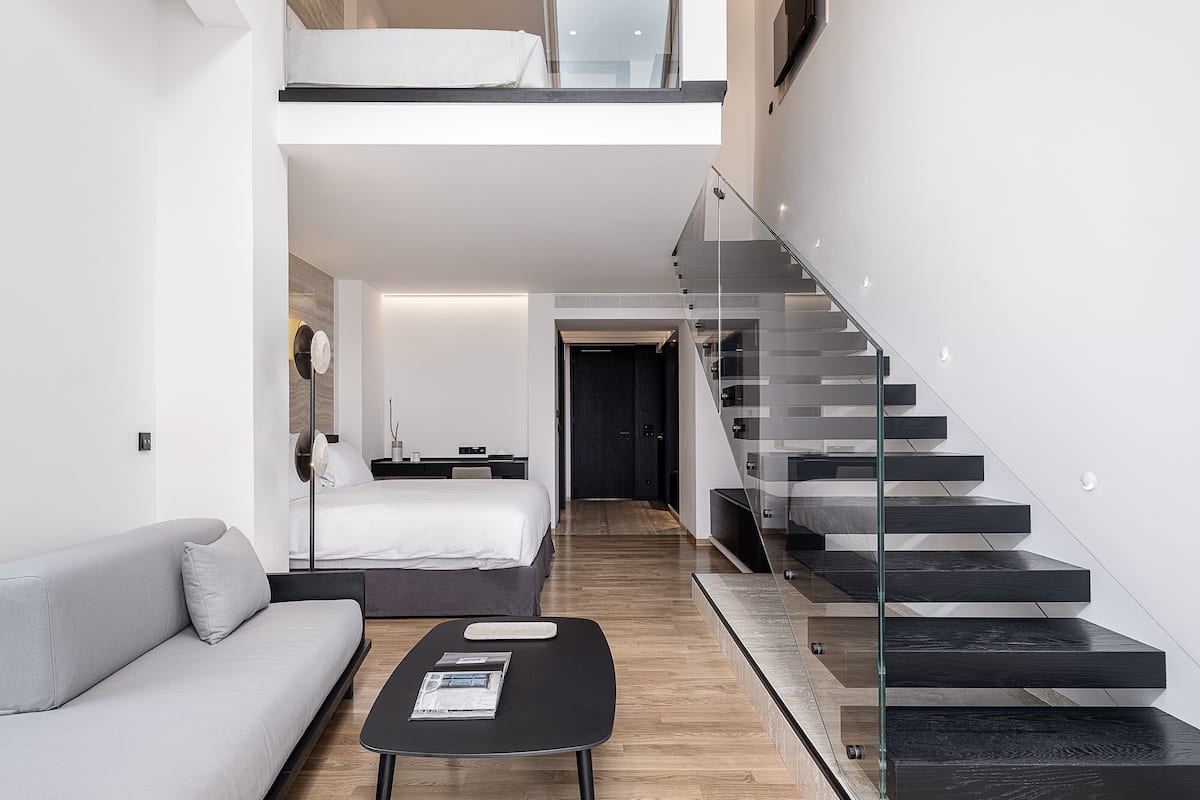 A modern living room with a sofa, a coffee table, and a staircase with glass railings.