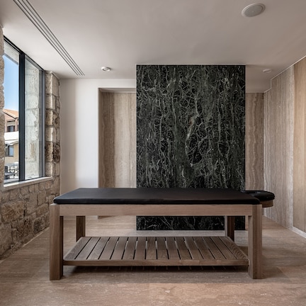 A modern interior with a wooden table and bench, a stone wall, and a large window.
