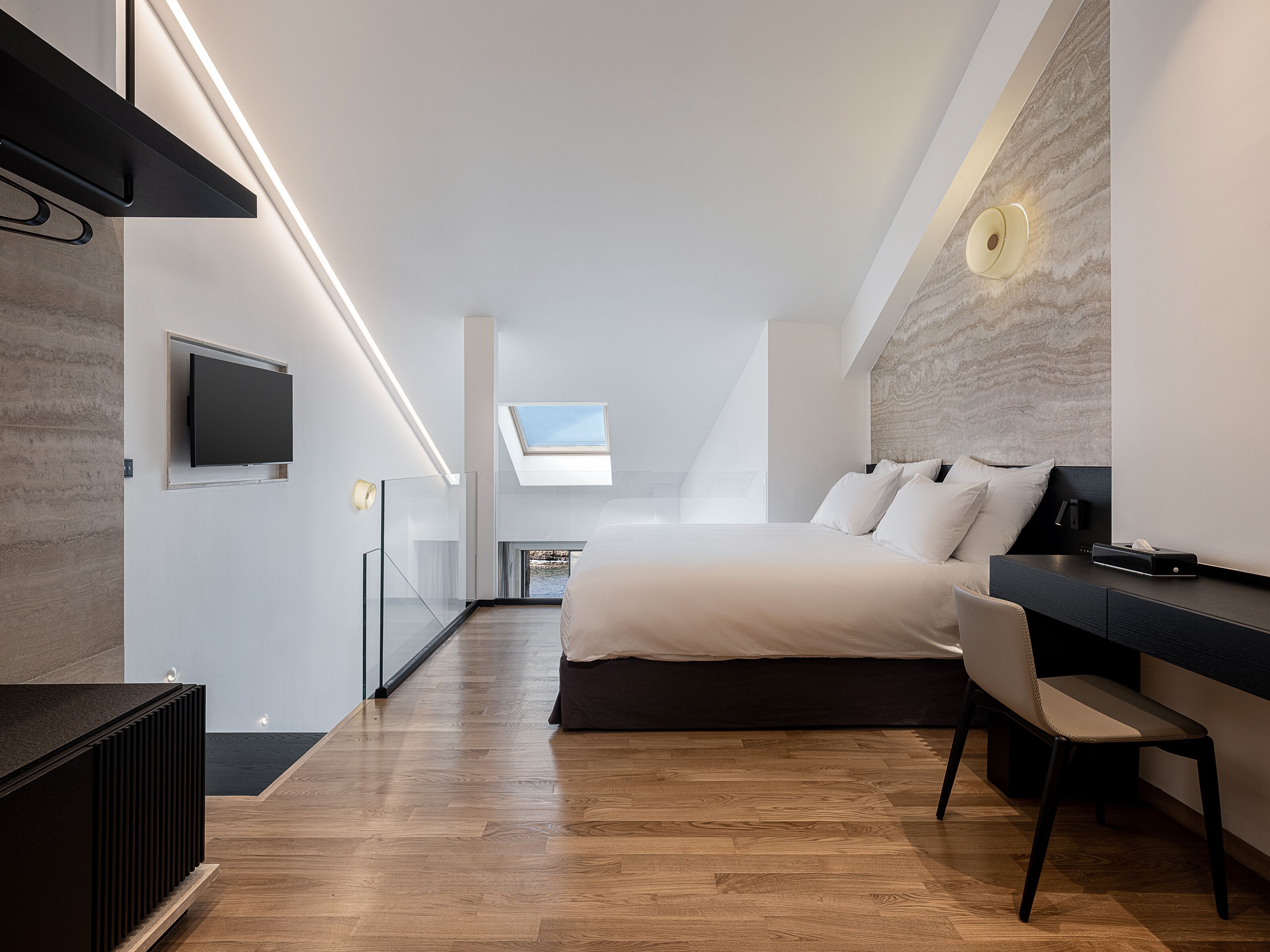 A modern bedroom with a large bed, a desk, and a television.