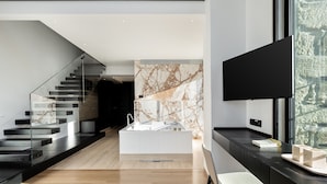 A modern interior with a staircase, a kitchen area, and a seating area with a TV.