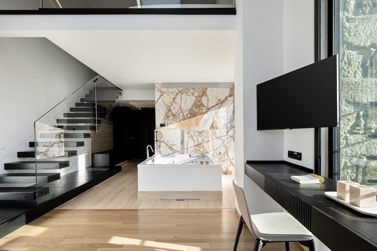 A modern interior with a staircase, a kitchen area, and a seating area with a TV.