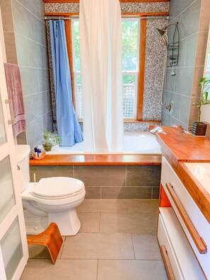 A bathroom with a toilet, shower, and bathtub. There is a window with a curtain, and a plant on the counter. - Lil' Bull Bungalow- walk to Duke, Downtown Durham & Food (Durham)