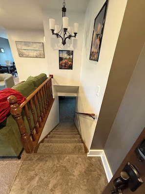 A staircase with a wooden handrail, carpeted steps, and a chandelier.