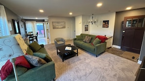 A living room with two green sofas, a coffee table, and a dining area in the background.