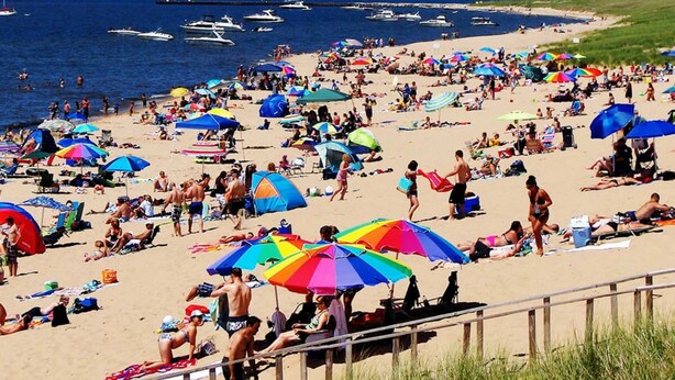 A crowded beach with numerous colorful umbrellas and people enjoying the sunny weather.