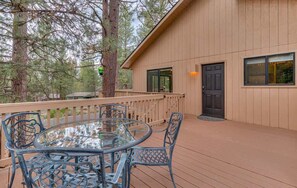 A wooden deck with a glass table and chairs, surrounded by trees. - Rustic family cabin, games, ac, shuffleboard (Sunriver)