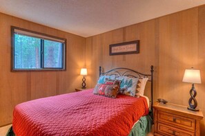 A bedroom with a large bed, a window with a view of trees, a bedside table with a lamp, and a framed quote on the wall. - Rustic family cabin, games, ac, shuffleboard (Sunriver)