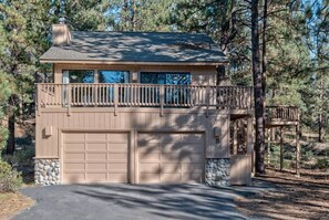 A two-story house with a balcony, two garage doors, and a stone foundation. - Rustic family cabin, games, ac, shuffleboard (Sunriver)