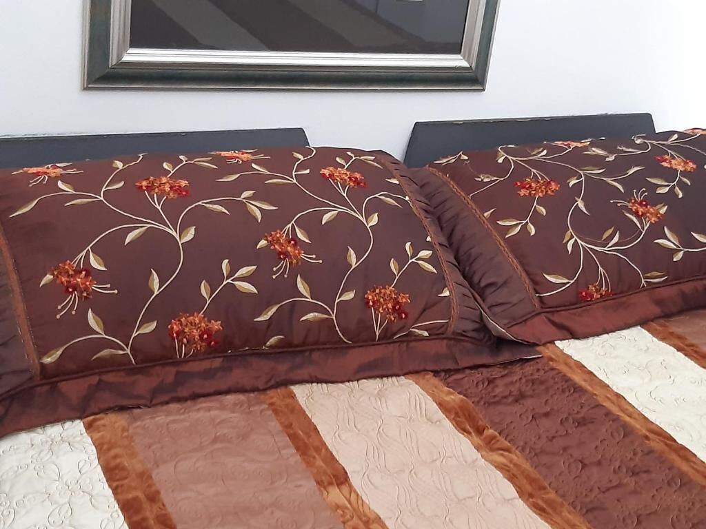 Uma cama com duas almofadas decorativas com padrão floral, um cobertor listrado e um quadro na parede.