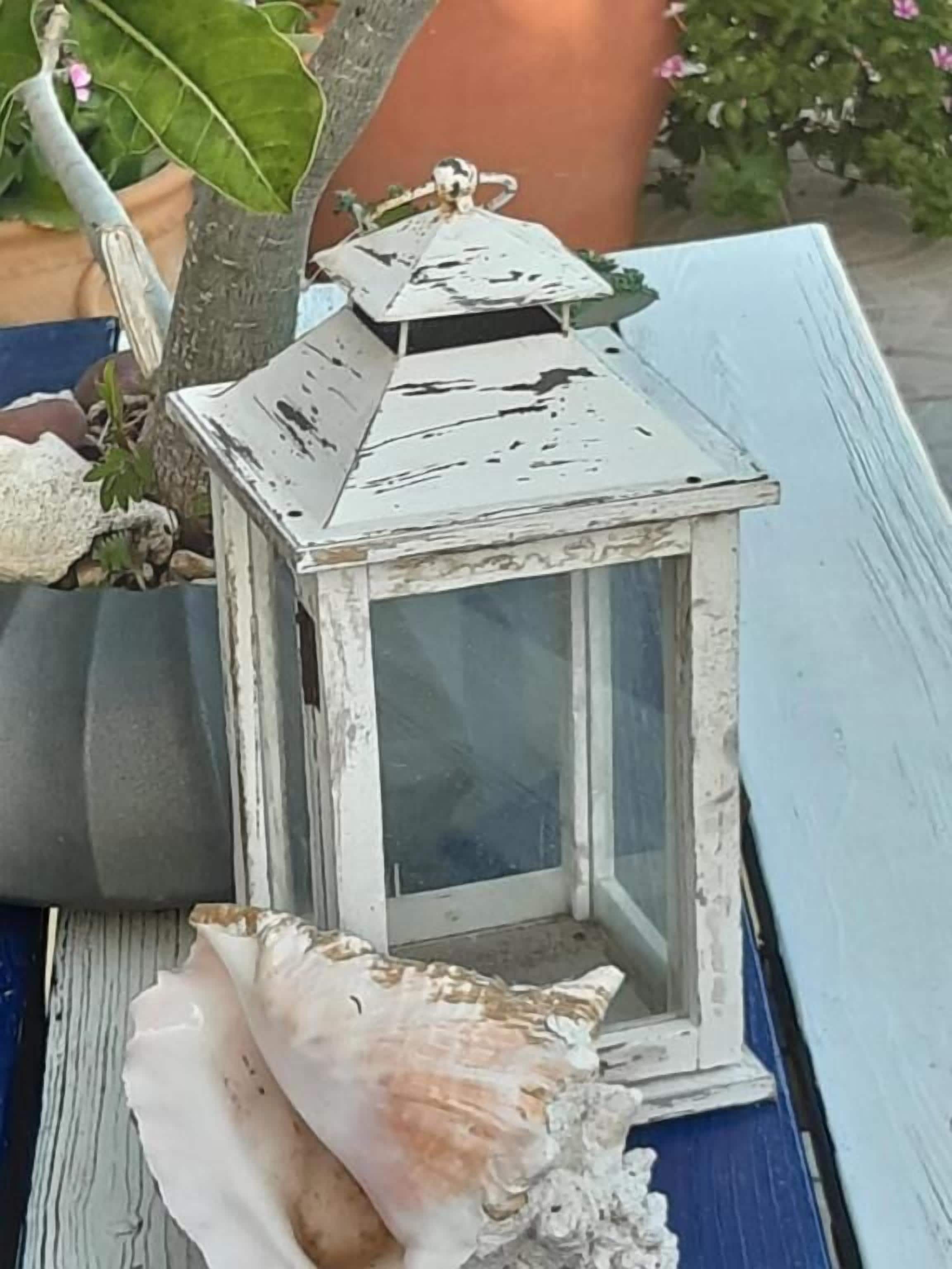 Un farol rústico con un diseño desgastado, sobre una superficie de madera con una concha marina cerca.