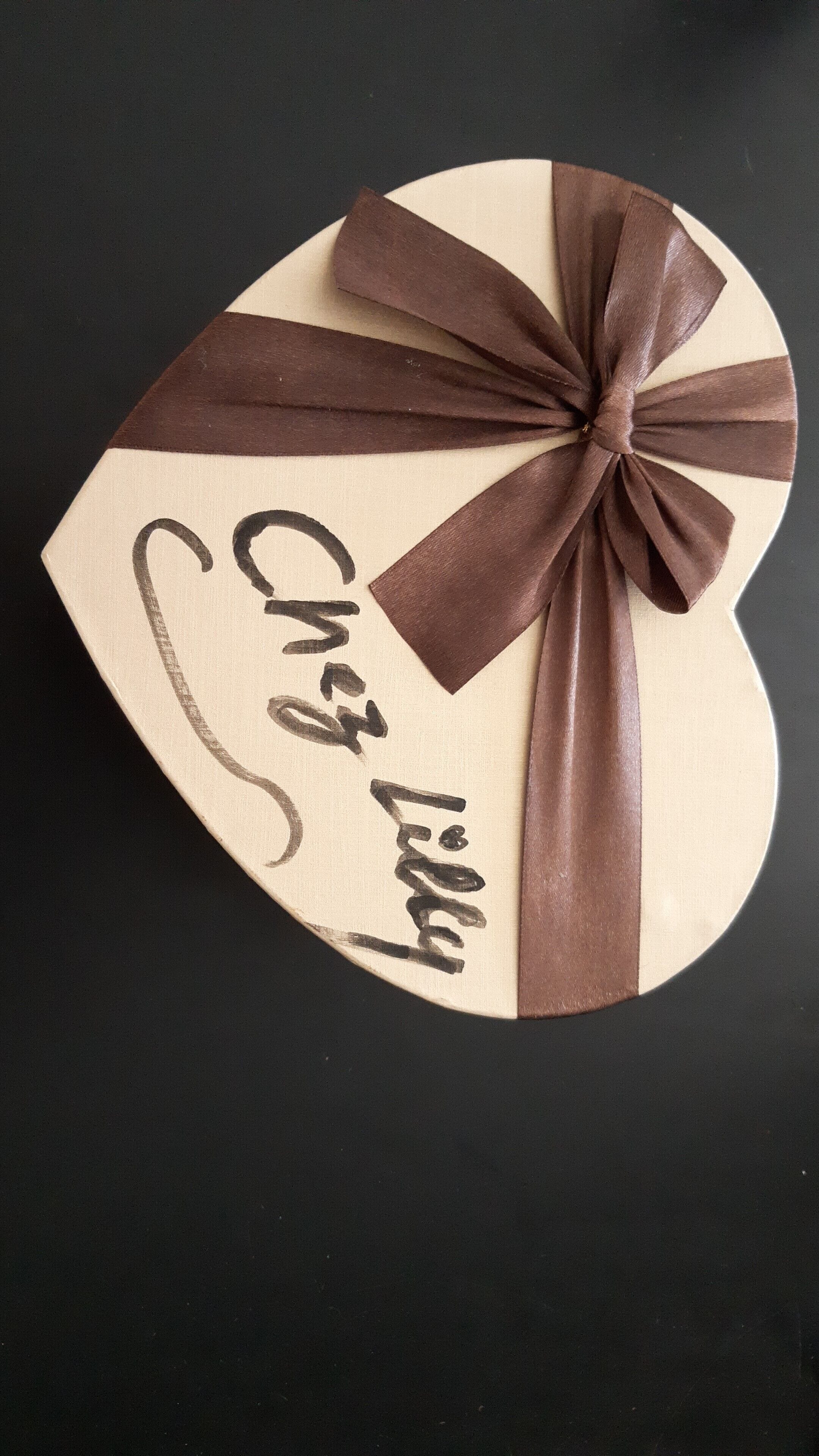 Un regalo con forma de corazón, con un lazo marrón y la inscripción 'Cher Lili'.