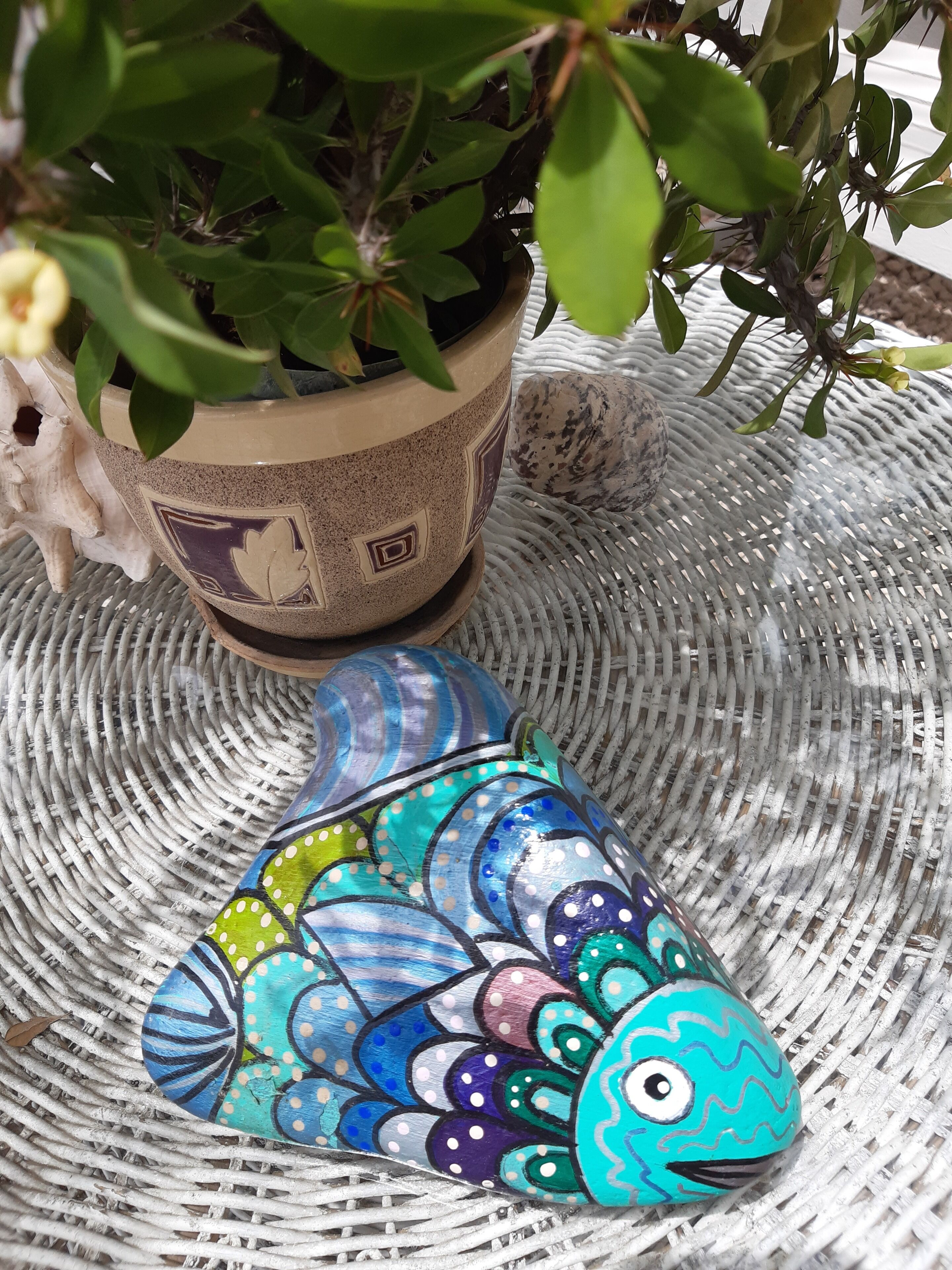 A potted plant with green leaves and a decorative ceramic fish on a woven surface.