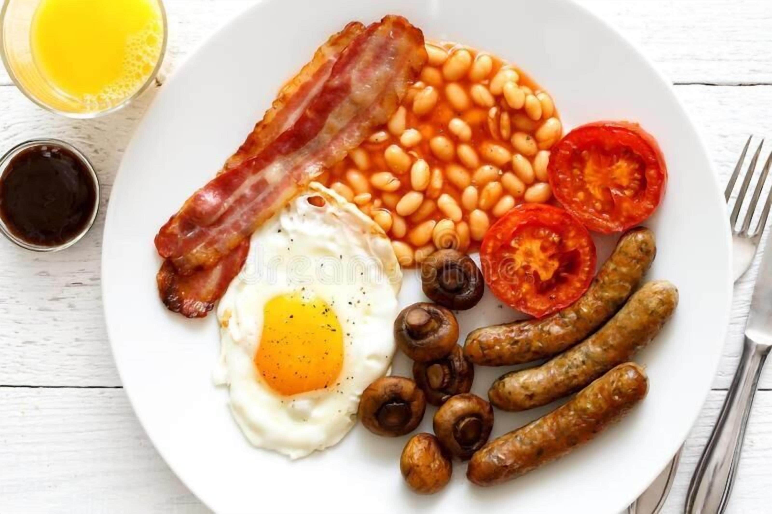 Un plato con tocino, frijoles, tomates, champiñones, salchichas y un huevo frito.