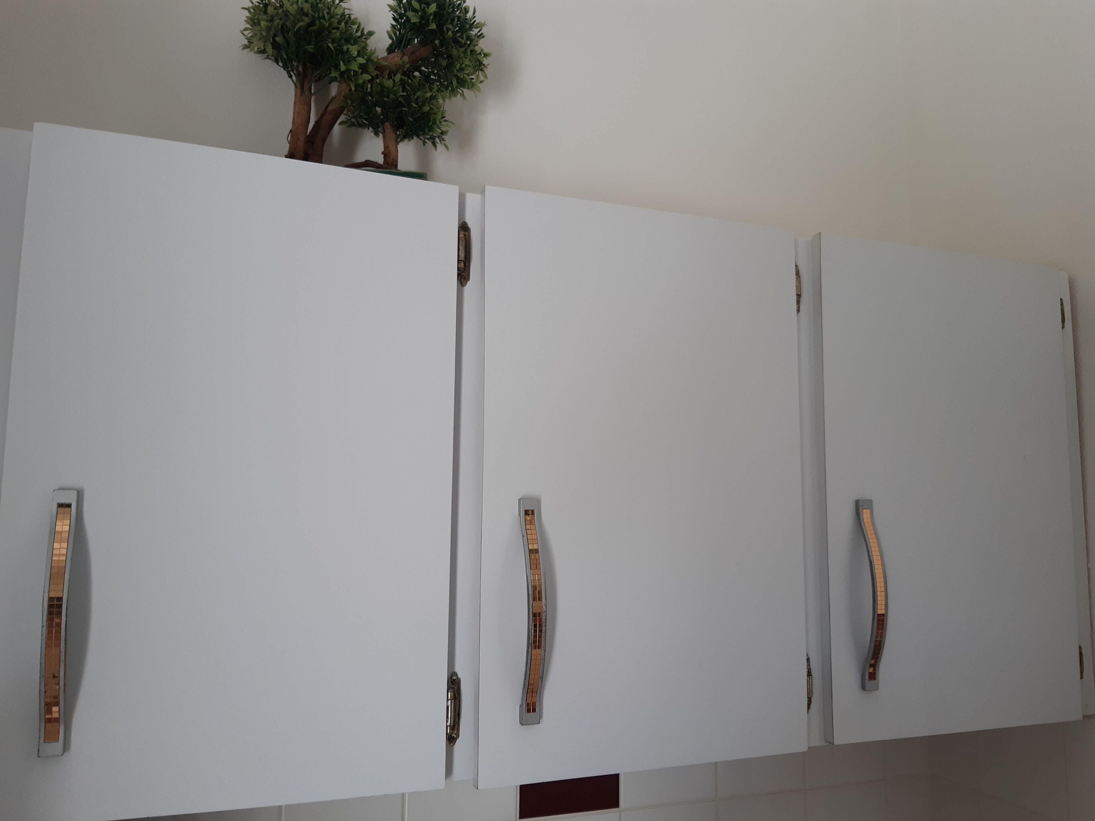 A set of white cabinets with metallic handles and a small artificial tree on top.