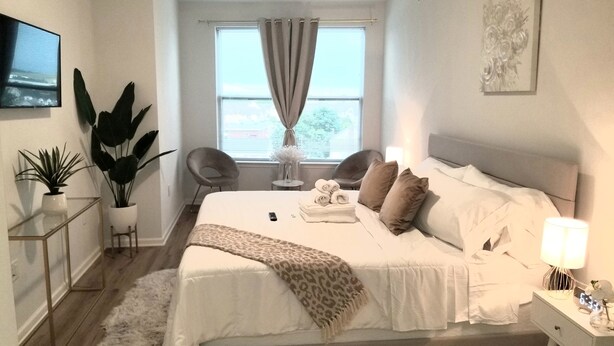 Ein modernes Schlafzimmer mit einem großen Bett, Nachttischen, einem Fernseher und Meerblick durch das Fenster.