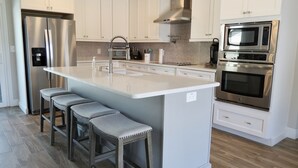 A modern kitchen with white cabinetry, stainless steel appliances, a central island with bar stools, and a wood floor. - Waterfront Retreat in the Heart of Tampa. Close to TPA, RayJay and Steinbrenner (Tampa)