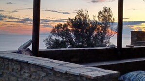 A stone bench with a view of the sea and trees at sunset.