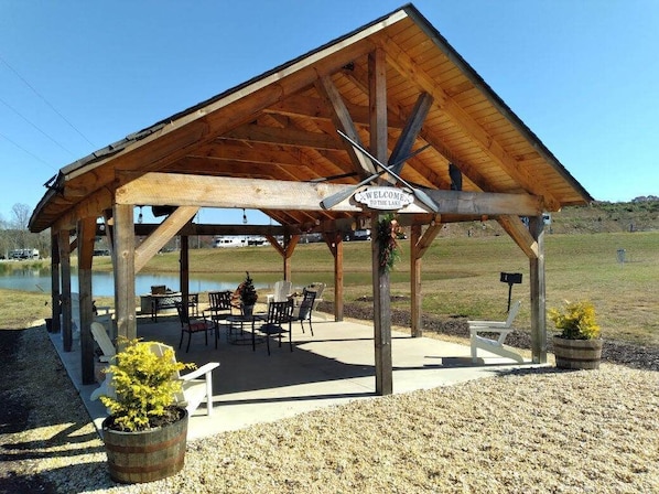 A wooden pavilion with a 'Welcome to the Lake' sign, outdoor seating, and a view of the lake.