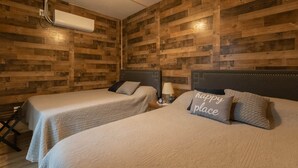 A room with two beds, wooden walls, a ceiling fan, and an air conditioning unit.