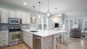 A modern kitchen with stainless steel appliances, a central island, and pendant lighting. - Mermaid Manor - with 6-seater Golf Cart! (Miramar Beach)