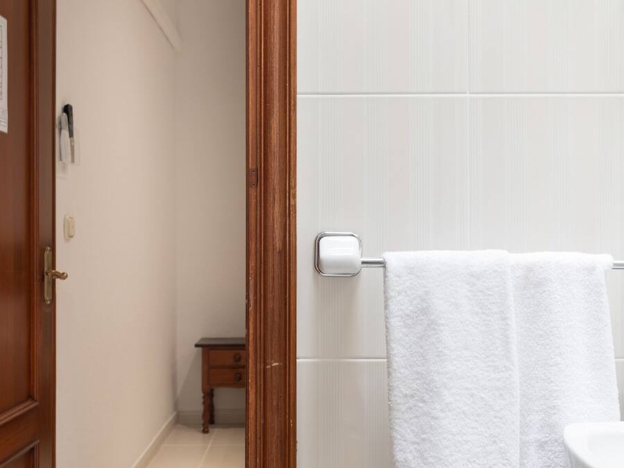 Un baño con paredes de azulejos blancos, una puerta de madera y un perchero con dos toallas blancas.