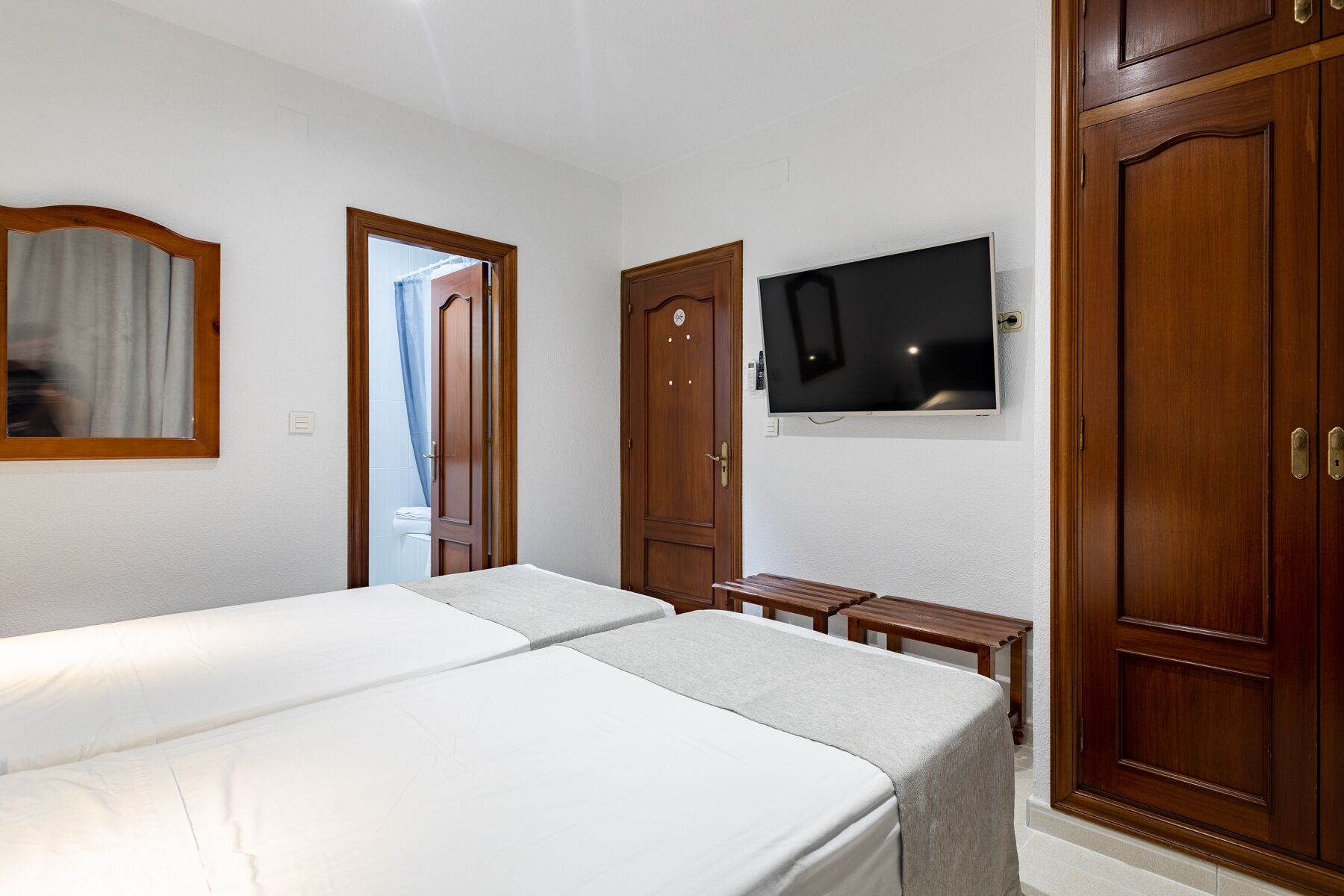 A hotel room with two beds, wooden wardrobes, a television, and a small table.
