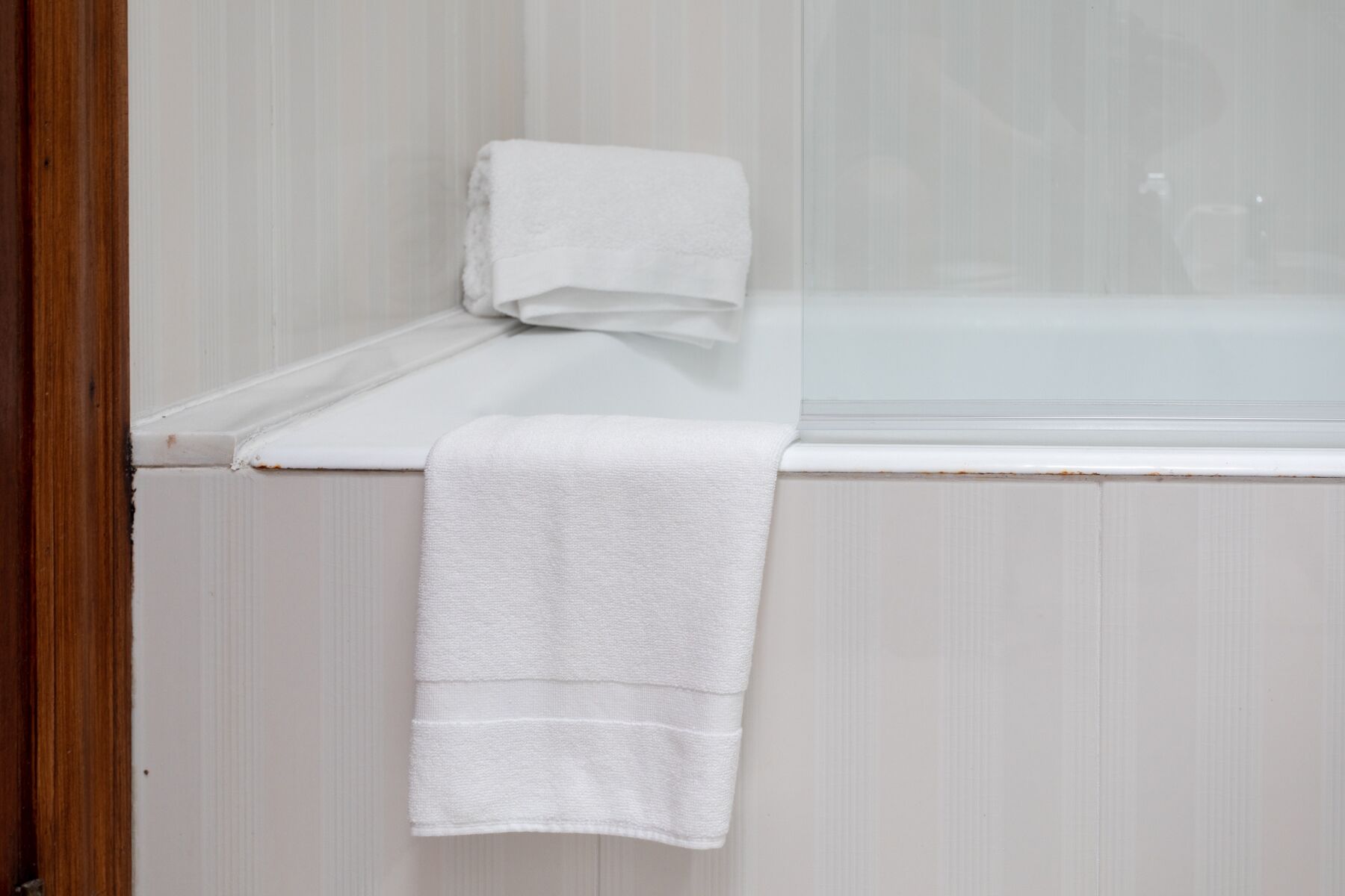 A bathroom with a white bathtub, a white towel on the edge, and a wooden door frame.
