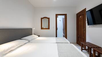 A hotel room with two beds, a wooden bench, a TV mounted on the wall, and a mirror above the bed.