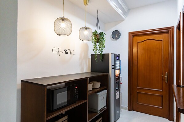A kitchen with a microwave, a coffee machine, and a clock on the wall. - Hostal La Costa (El Ejido)