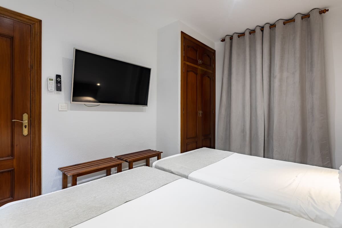 A hotel room with two beds, a TV mounted on the wall, wooden wardrobes, and a curtain.