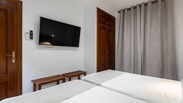 Une chambre d’hôtel avec deux lits, un téléviseur fixé au mur, des armoires en bois et un rideau.