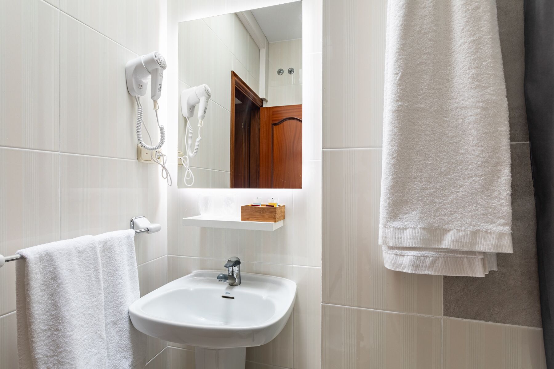 Un baño con lavamanos blanco, espejo, secador de pelo y toallero.