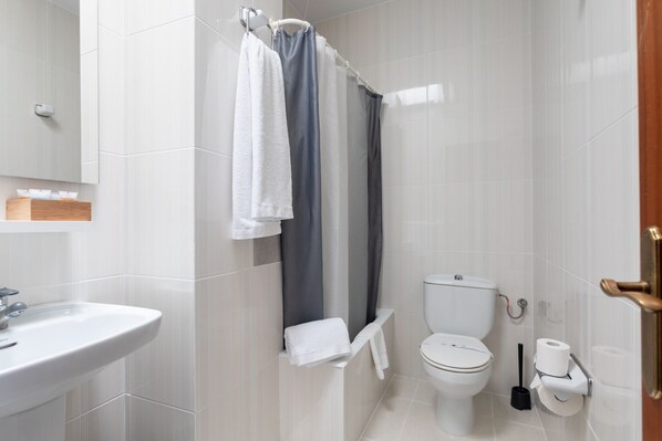 Un baño moderno con lavamanos, inodoro y zona de ducha blancos.