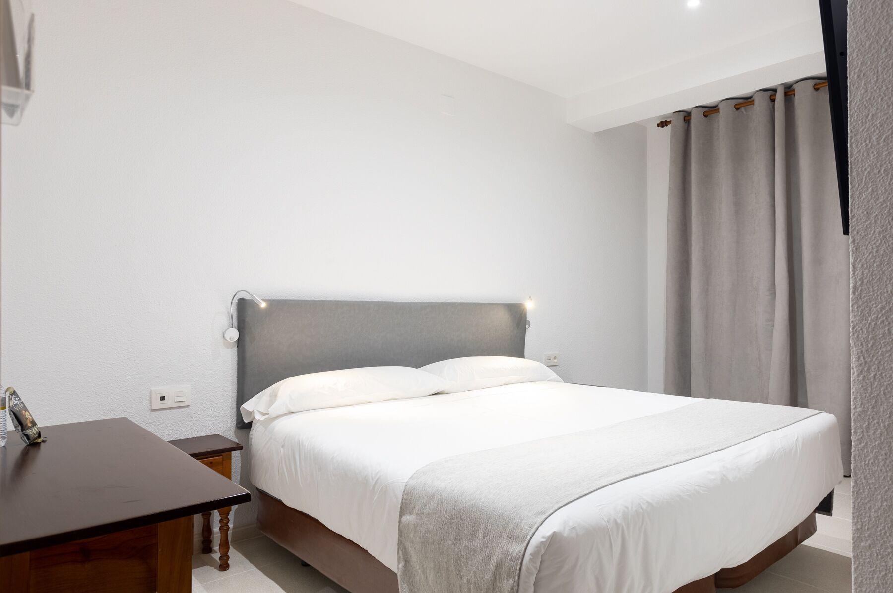 Une chambre d’hôtel avec un lit, une table de chevet, un bureau et une fenêtre avec des rideaux.