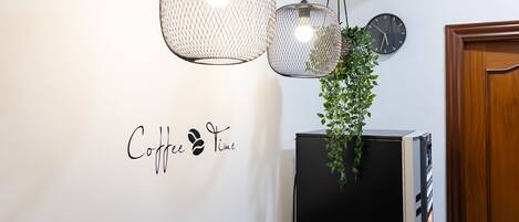 A wall with a "Coffee Time" sign, two hanging pendant lights, a clock, and a potted plant.