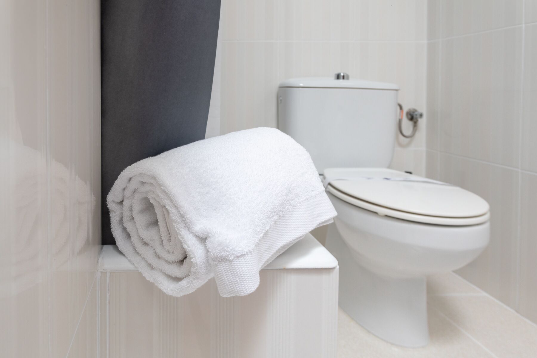 Een wit toilet met een handdoek ernaast in een badkamer met witte tegels.
