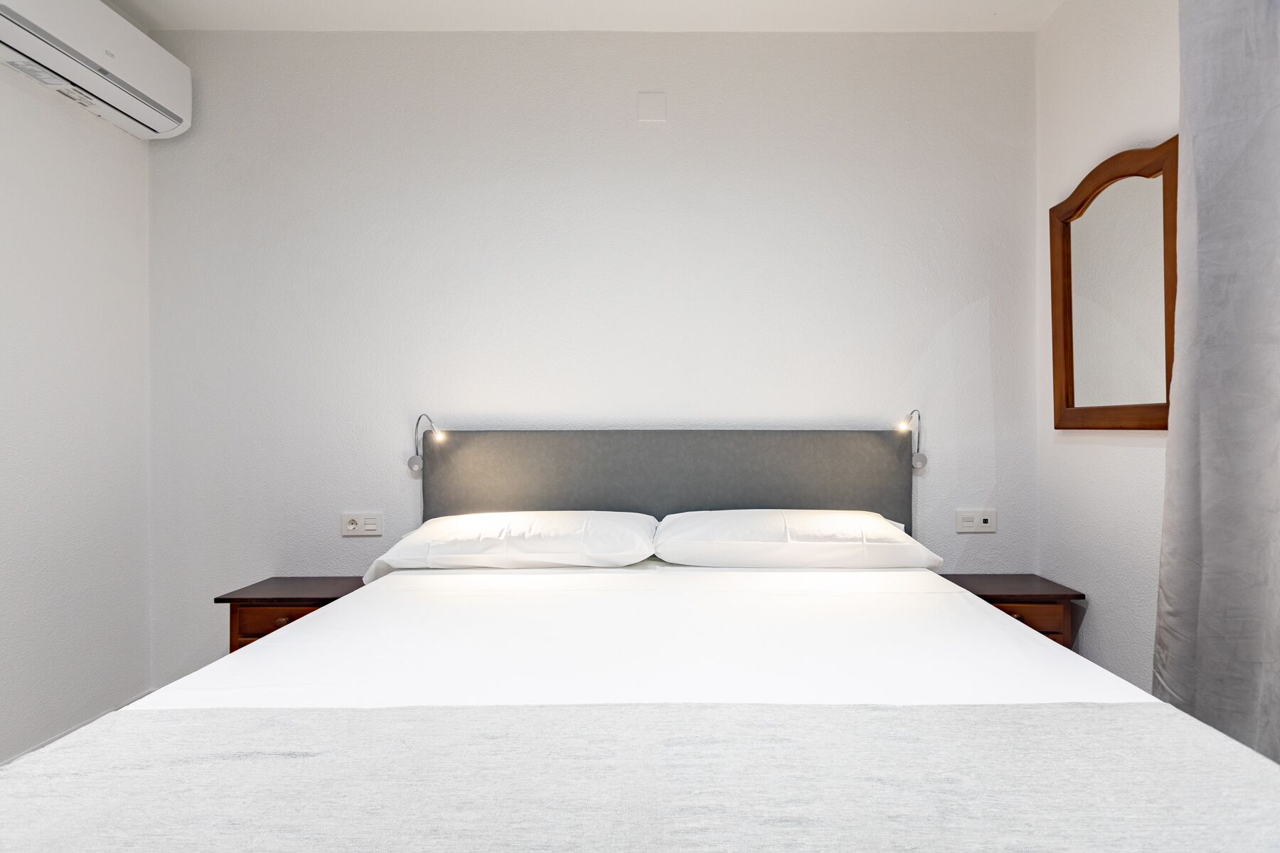 A minimalist bedroom with a large bed, two bedside tables, and a wall-mounted mirror.