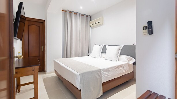 A bedroom with a bed, a wooden desk, a chair, an air conditioning unit, and a telephone. - Hostal La Costa (El Ejido)