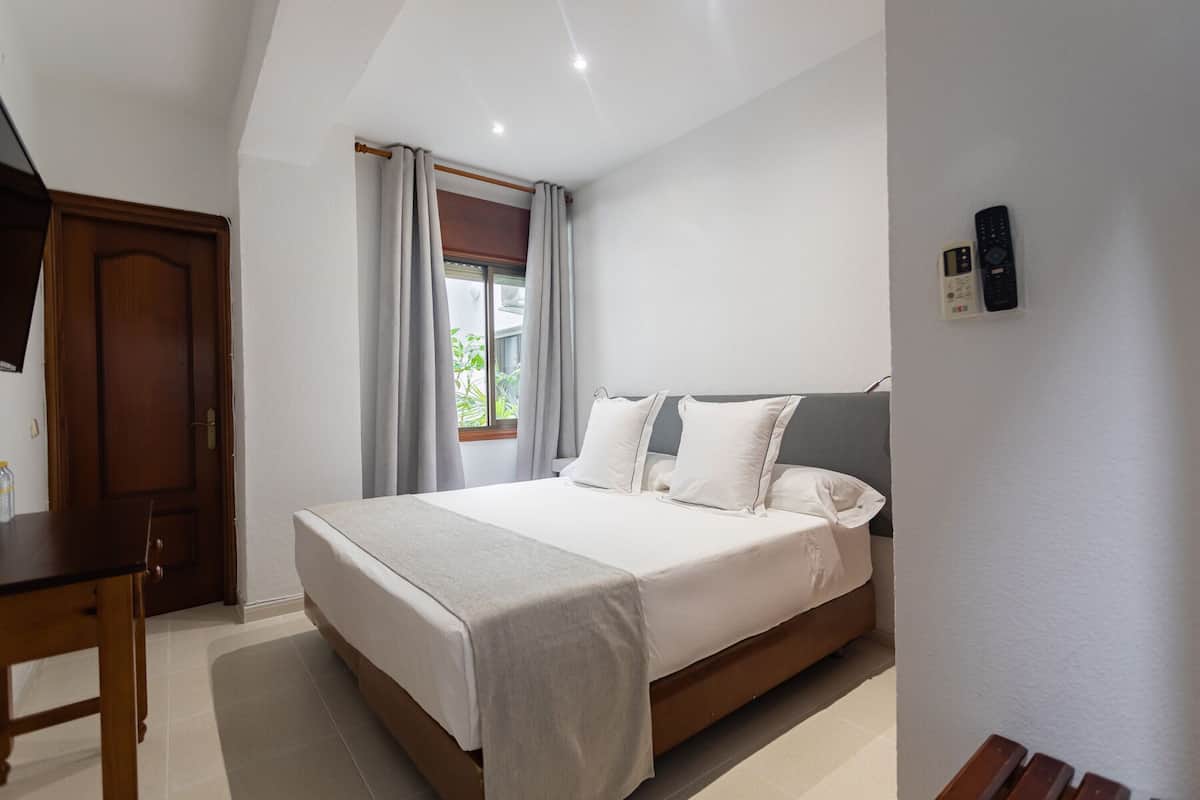 A bedroom with a bed, a desk, and a window with curtains.