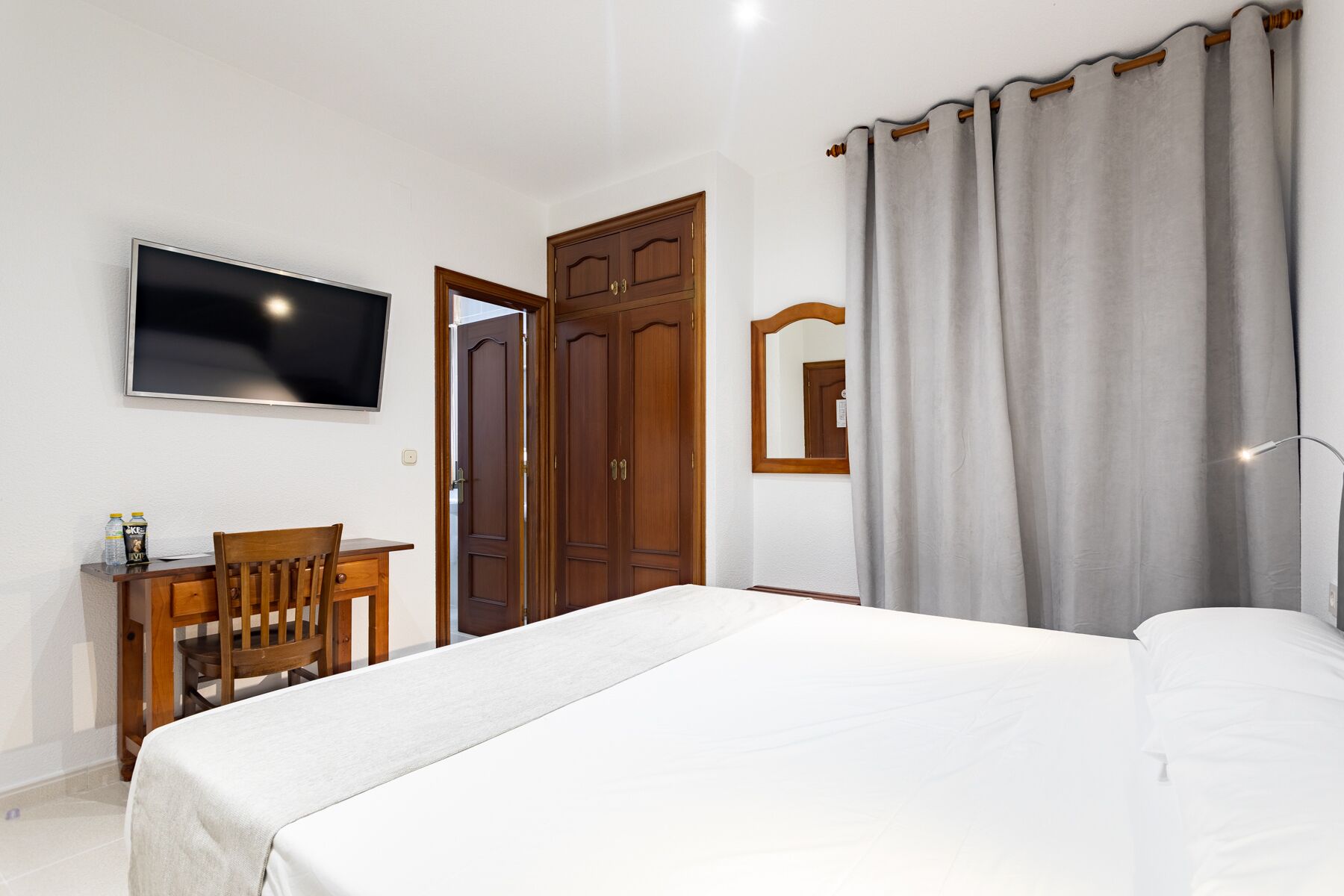A bedroom with a bed, a desk with a chair, a television, and a wardrobe.
