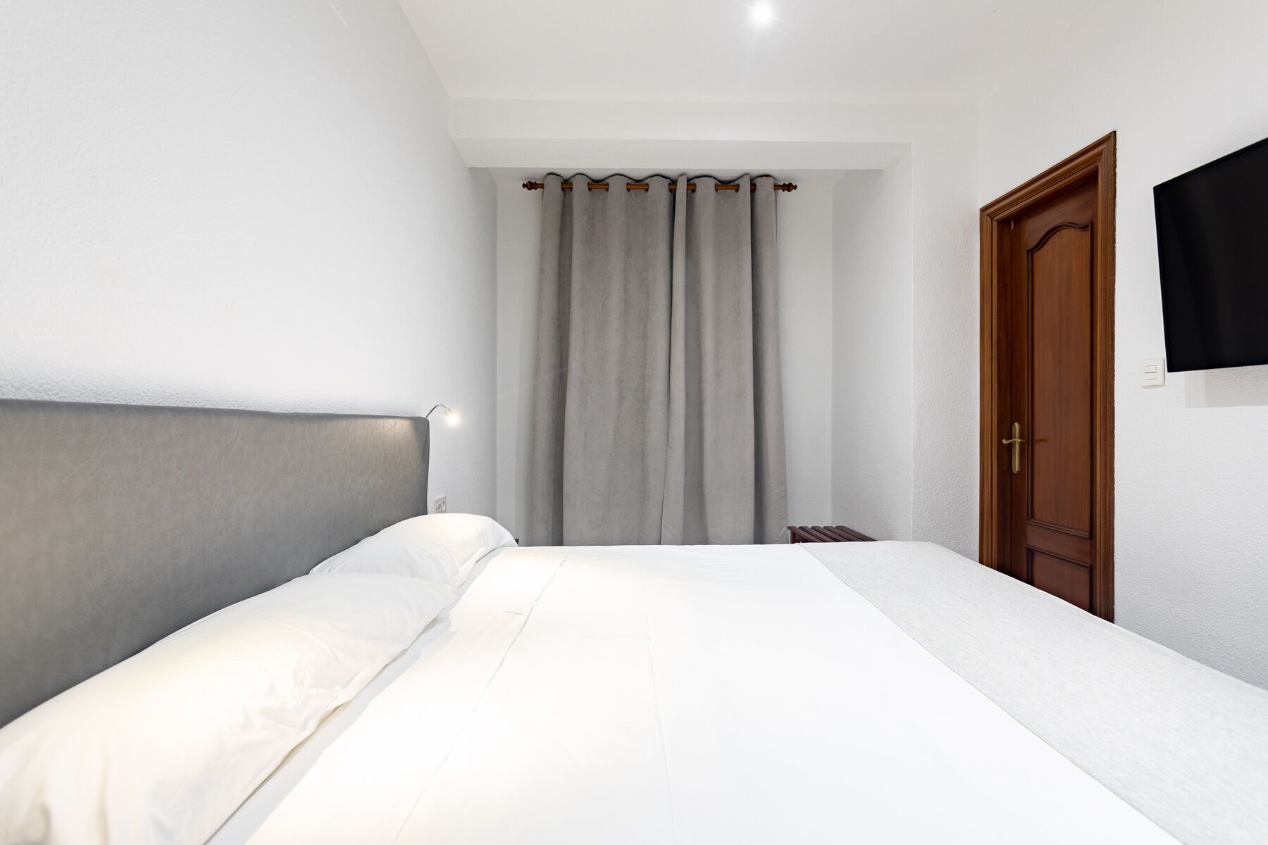 Un dormitorio con una cama, una puerta de madera y una cortina.