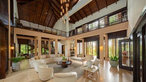 A spacious living area with a high ceiling, a central seating arrangement, and large windows allowing natural light. - Casa Yaya - Ocean view villa with chef, staff, golf cart, heated pool & jacuzzi (Punta Cana)