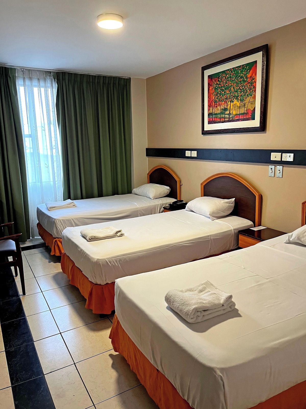 A hotel room with two beds, a painting on the wall, and a window with curtains.