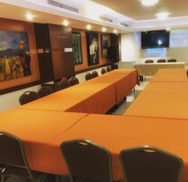 Un salón de conferencias con largas mesas, sillas y una pantalla grande.