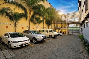 Un estacionamiento con varios coches, la entrada de un edificio y palmeras.