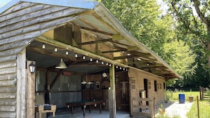 Un edificio rústico de madera con un área de estar al aire libre cubierta, una mesa de billar y un bar.