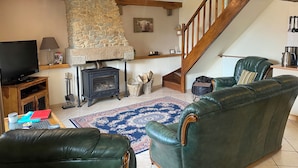 Una sala de estar acogedora con chimenea de piedra, sofás de cuero, televisión y una escalera.