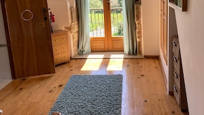 Una habitación con puerta de madera, un pequeño tapete, una cama, un aparador y un balcón con cortinas.